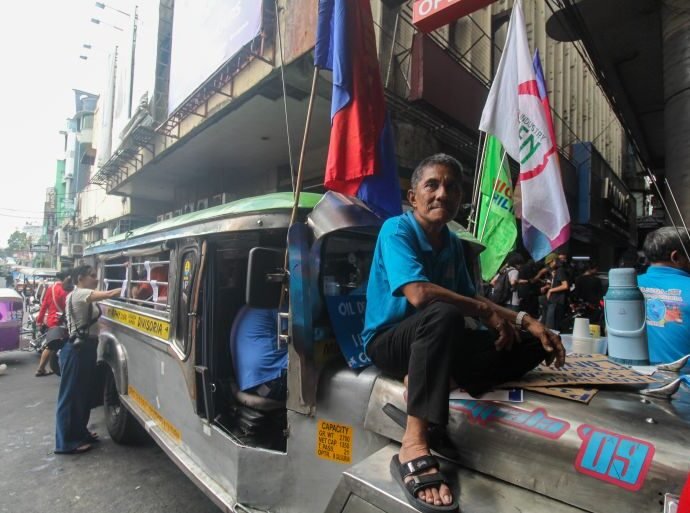 Driver sits atop his idle jeepney at a busy Manila transport hub. 1774677250